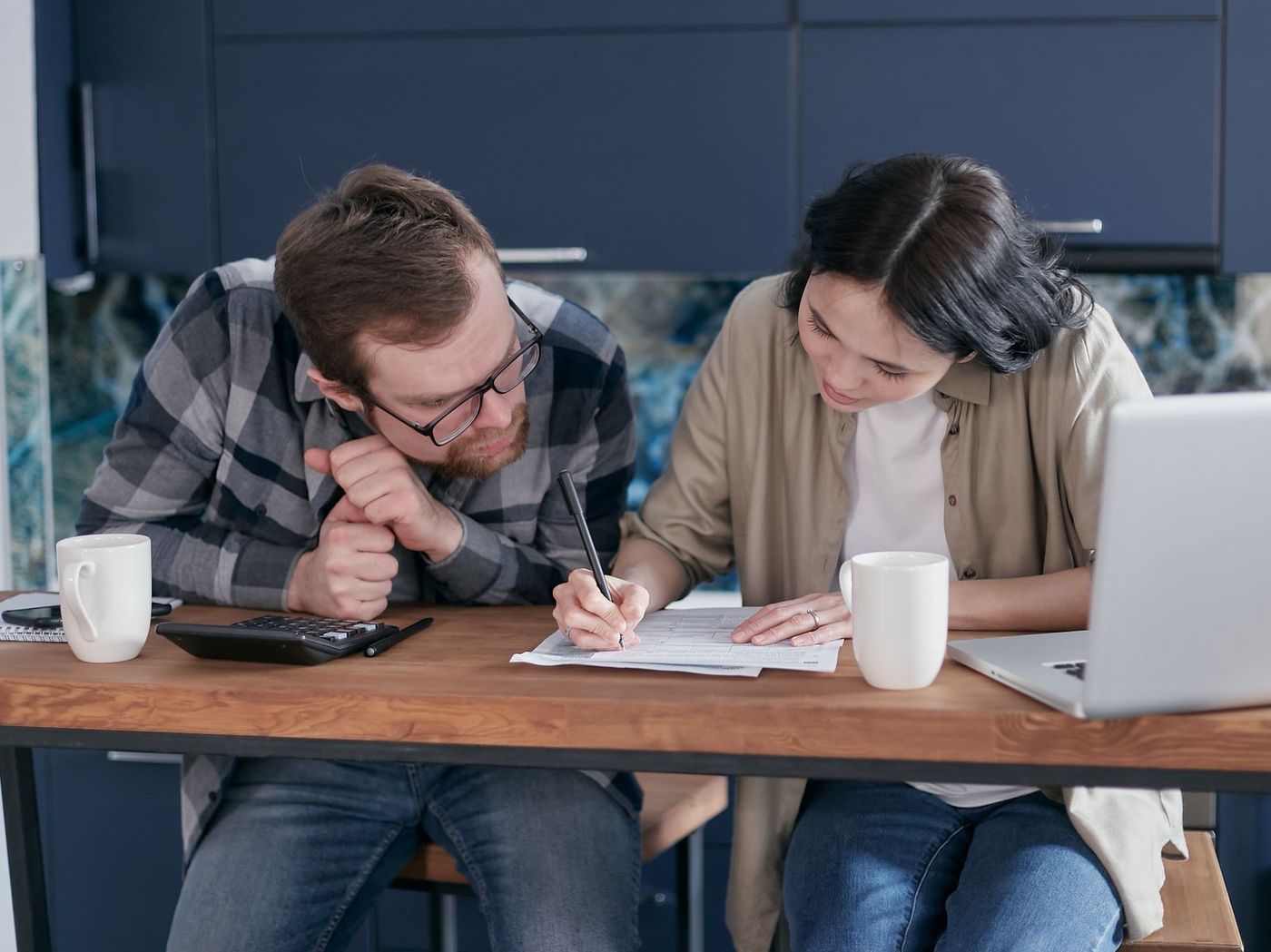 An adult daughter and her older father reviewing care funding paperwork together at a kitchen table with a laptop